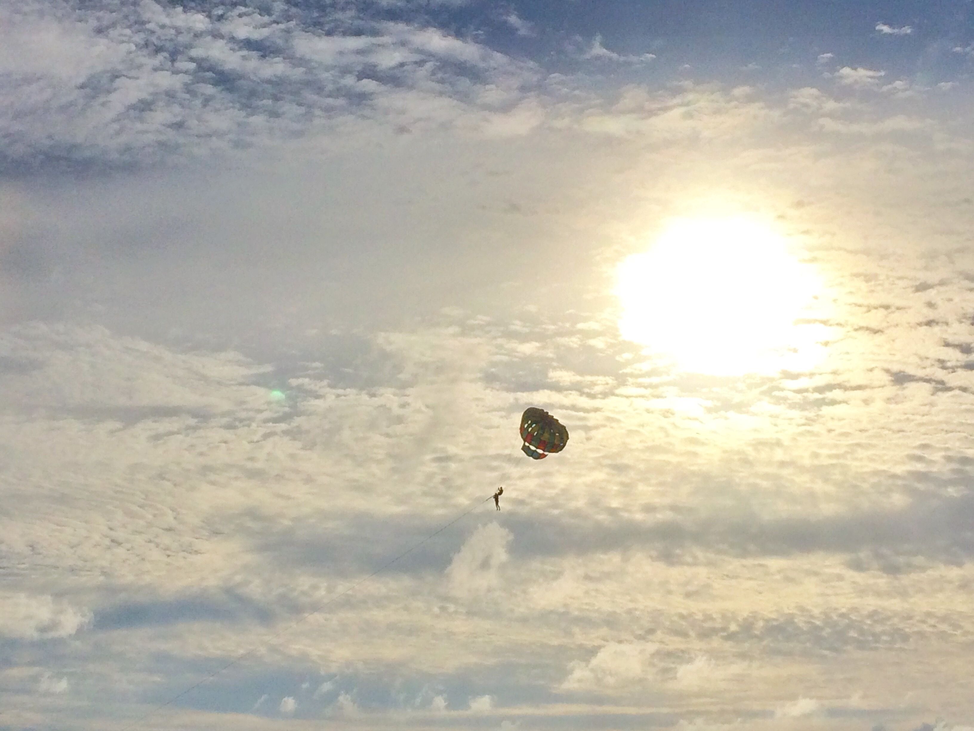 A person parachuting with a parachute against a sky with clouds and the sun.