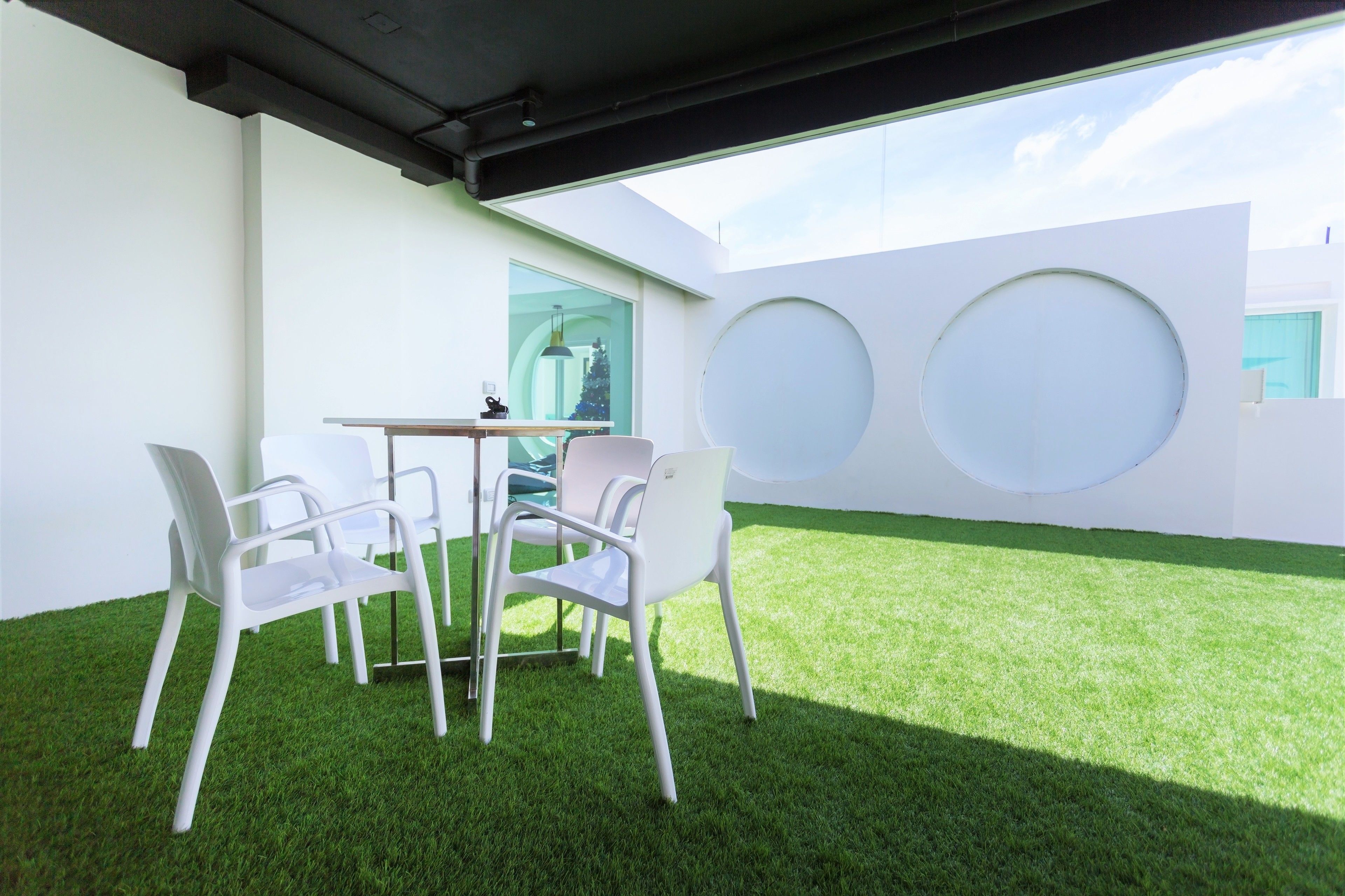 Un espacio moderno al aire libre con una mesa y cuatro sillas, rodeado de paredes blancas y un césped verde.