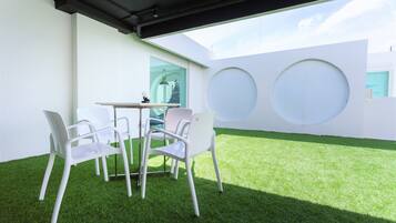 Un espacio moderno al aire libre con una mesa y cuatro sillas, rodeado de paredes blancas y un césped verde.