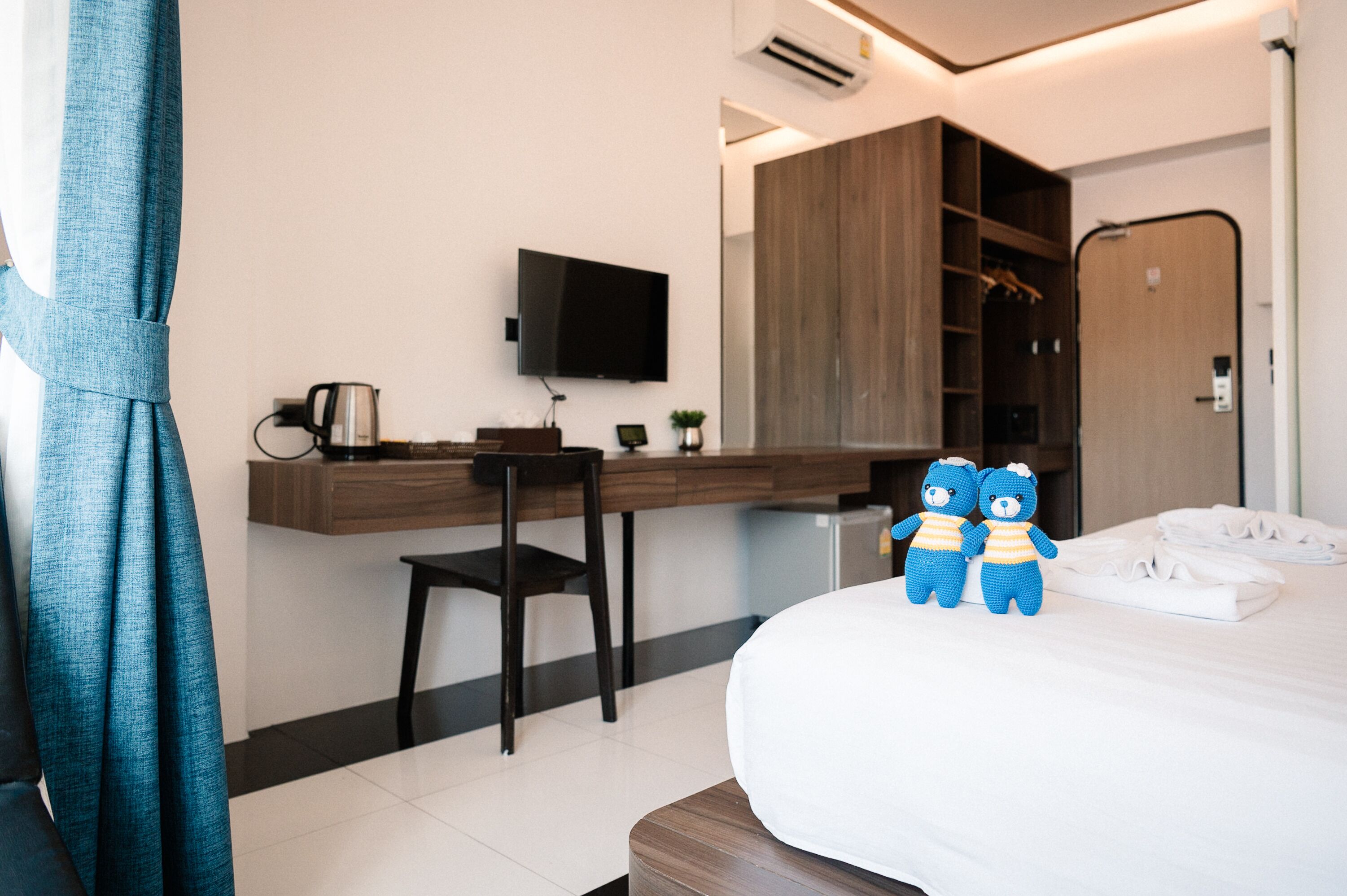Une chambre d’hôtel comprenant un lit, un bureau, une chaise, une télévision, une armoire et une paire de peluches.