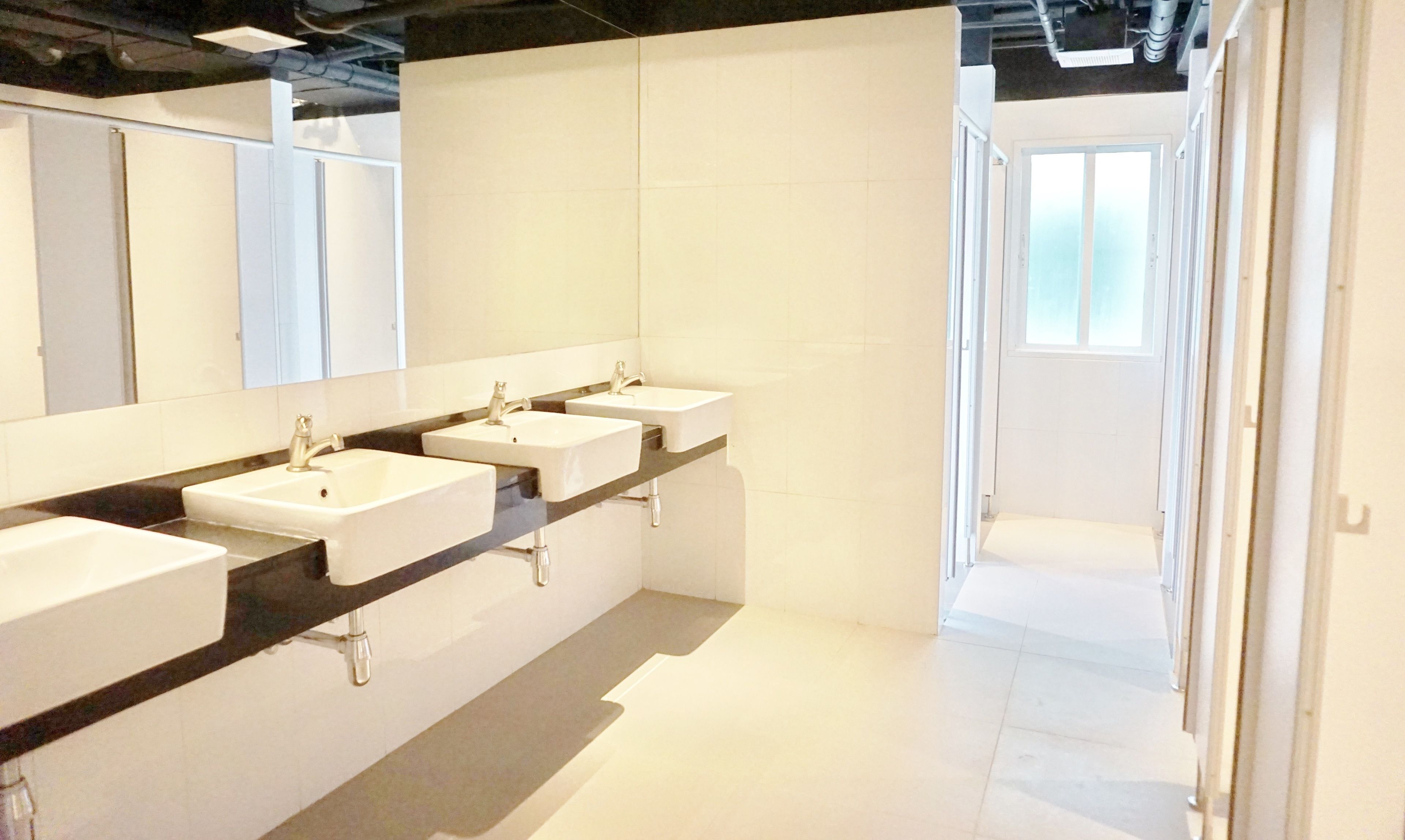 Un baño moderno con tres lavamanos, un espejo grande y una encimera negra.
