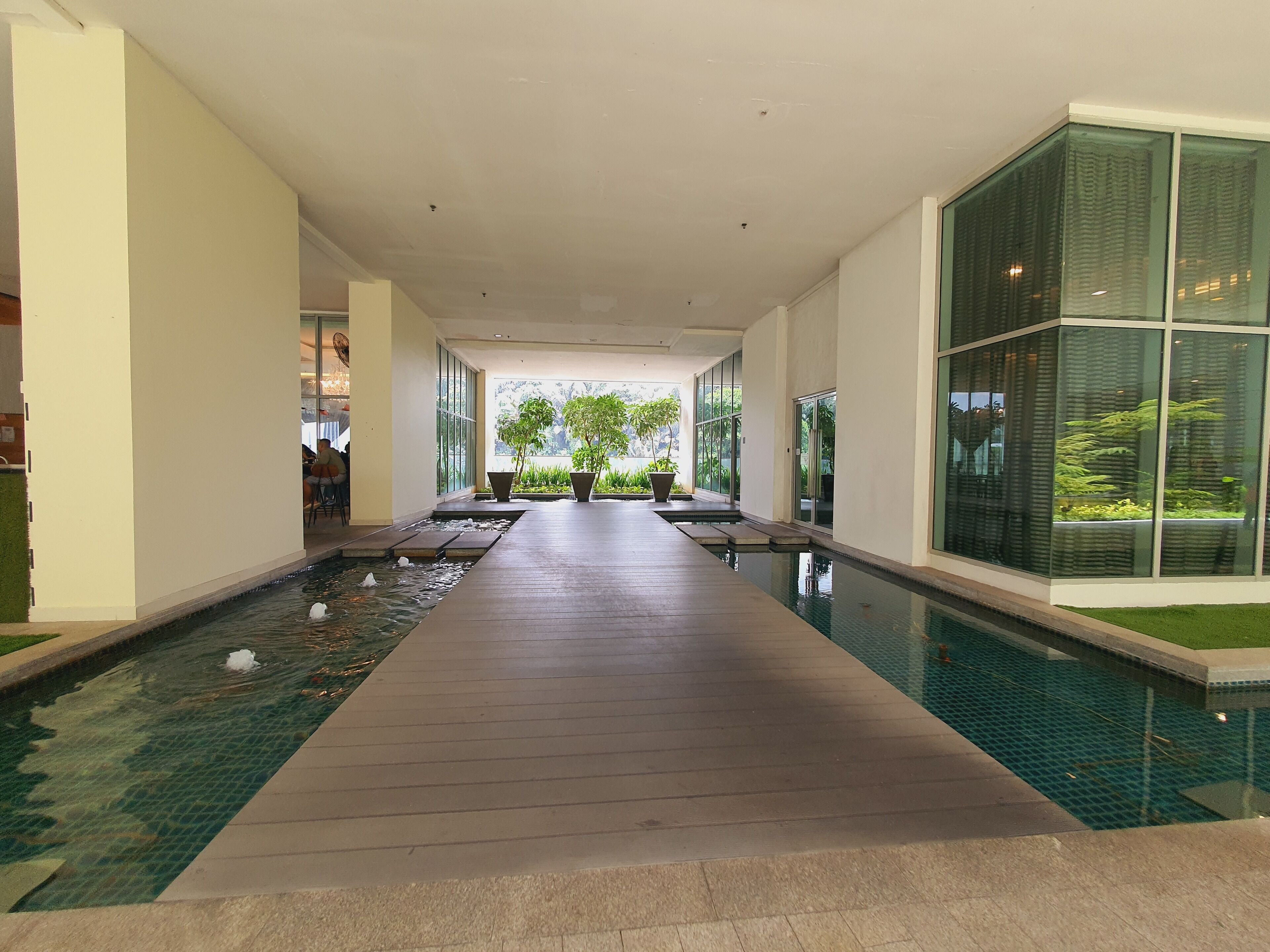 A modern indoor swimming pool with a wooden deck, large windows, and potted plants.
