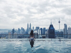 Une personne se tient dans une piscine, avec la silhouette d’une ville en arrière-plan.
