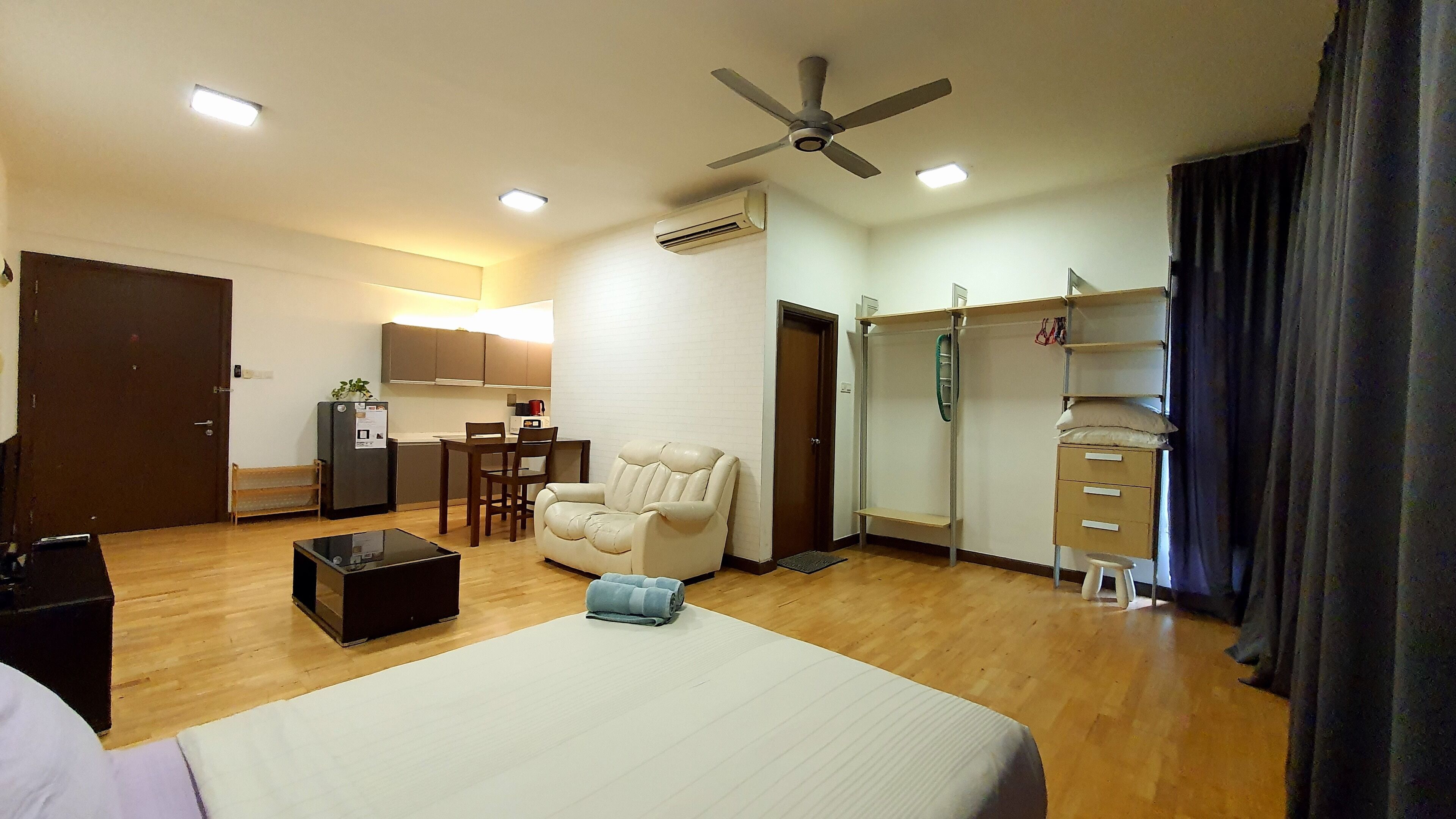 A hotel room with a bed, a desk, a chair, a sofa, a wardrobe, and a ceiling fan.