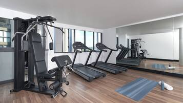 Un gimnasio moderno con cintas de correr, máquinas de pesas y un espejo grande.