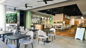Un restaurante moderno con mesas y sillas altas, zona de cocina y ventiladores de techo.