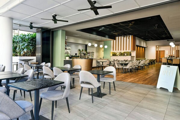 A modern restaurant with high tables and chairs, a kitchen area, and ceiling fans. - Courtyard by Marriott Brisbane South Bank (South Brisbane)