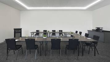 A conference room with a long table, black chairs, a podium, and a kitchenette area.