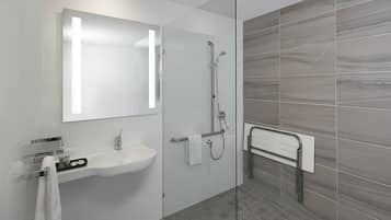 Un baño moderno con cabina de ducha de vidrio, un lavabo blanco con espejo y un perchero para toallas.