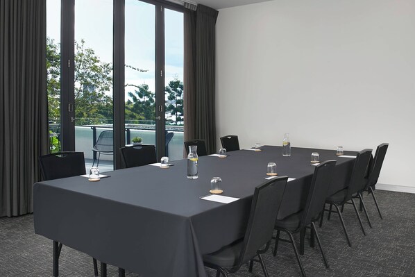 A conference room with a long table, black chairs, and a view through large windows. - Courtyard by Marriott Brisbane South Bank (South Brisbane)
