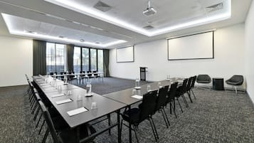 Uma sala de conferências com uma mesa comprida, cadeiras, uma tela de projetor e um grande janela com cortinas.