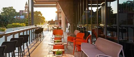 An outdoor seating area with tables and chairs, a wicker sofa, and a view of the cityscape.