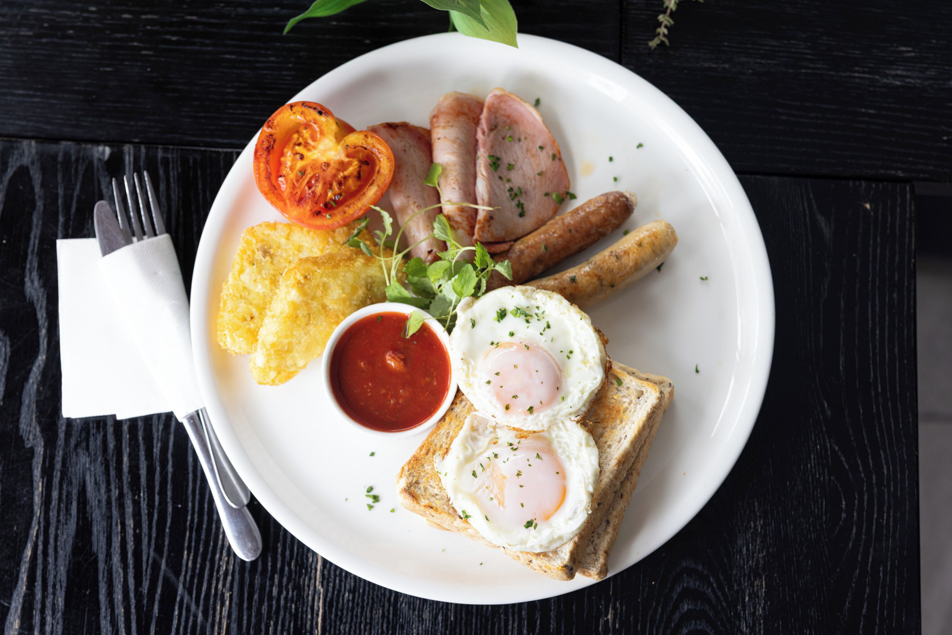 Un plato con alimentos para el desayuno, incluyendo huevos, salchichas y una rebanada de tomate.