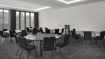 Un salón de conferencias con varias mesas y sillas, un atril y ventanas amplias con cortinas.