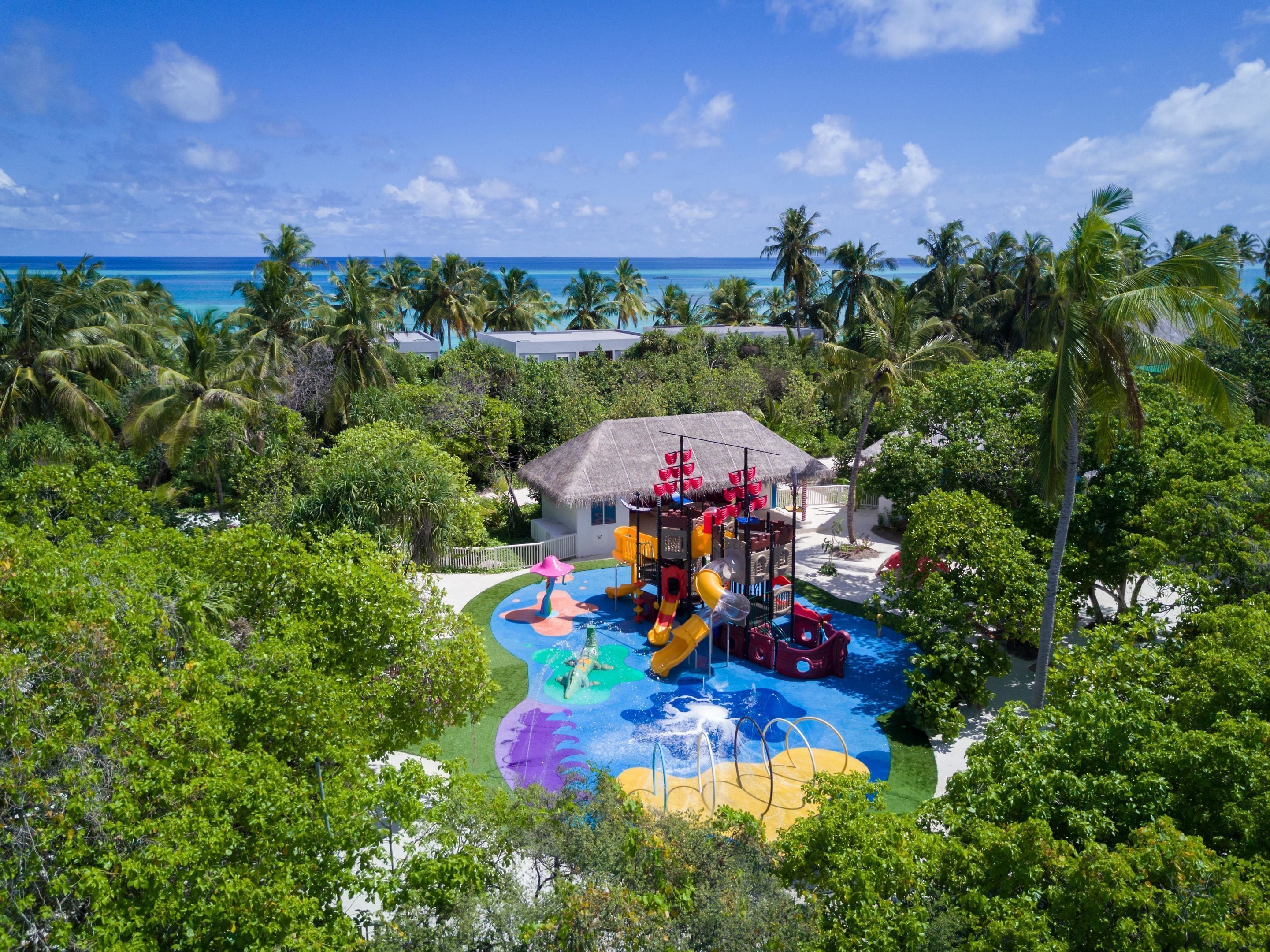 A water park with slides and a pool, surrounded by palm trees and a beach.