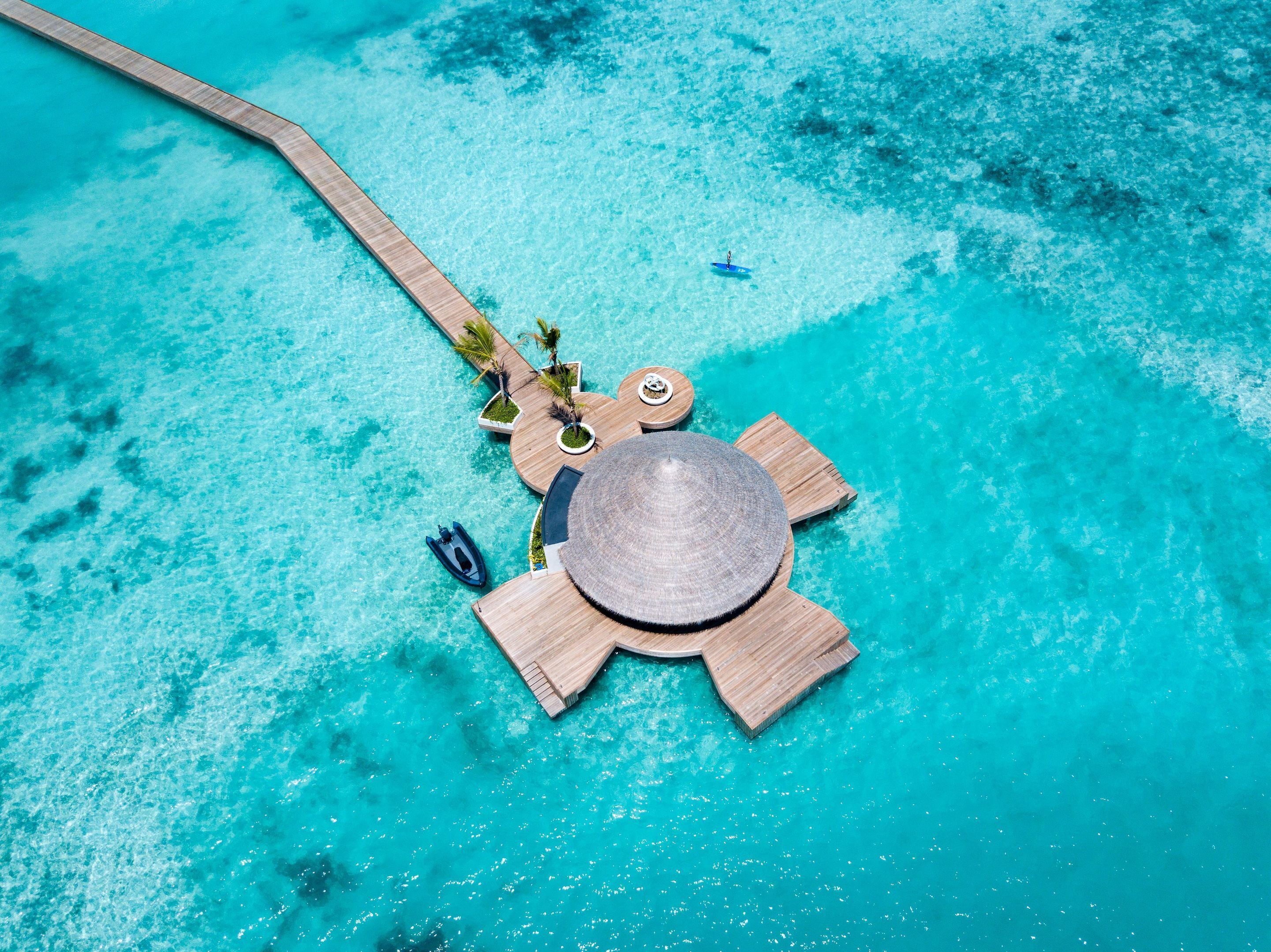 An aerial view of a tropical resort with a wooden deck, lounge chairs, and a small boat.
