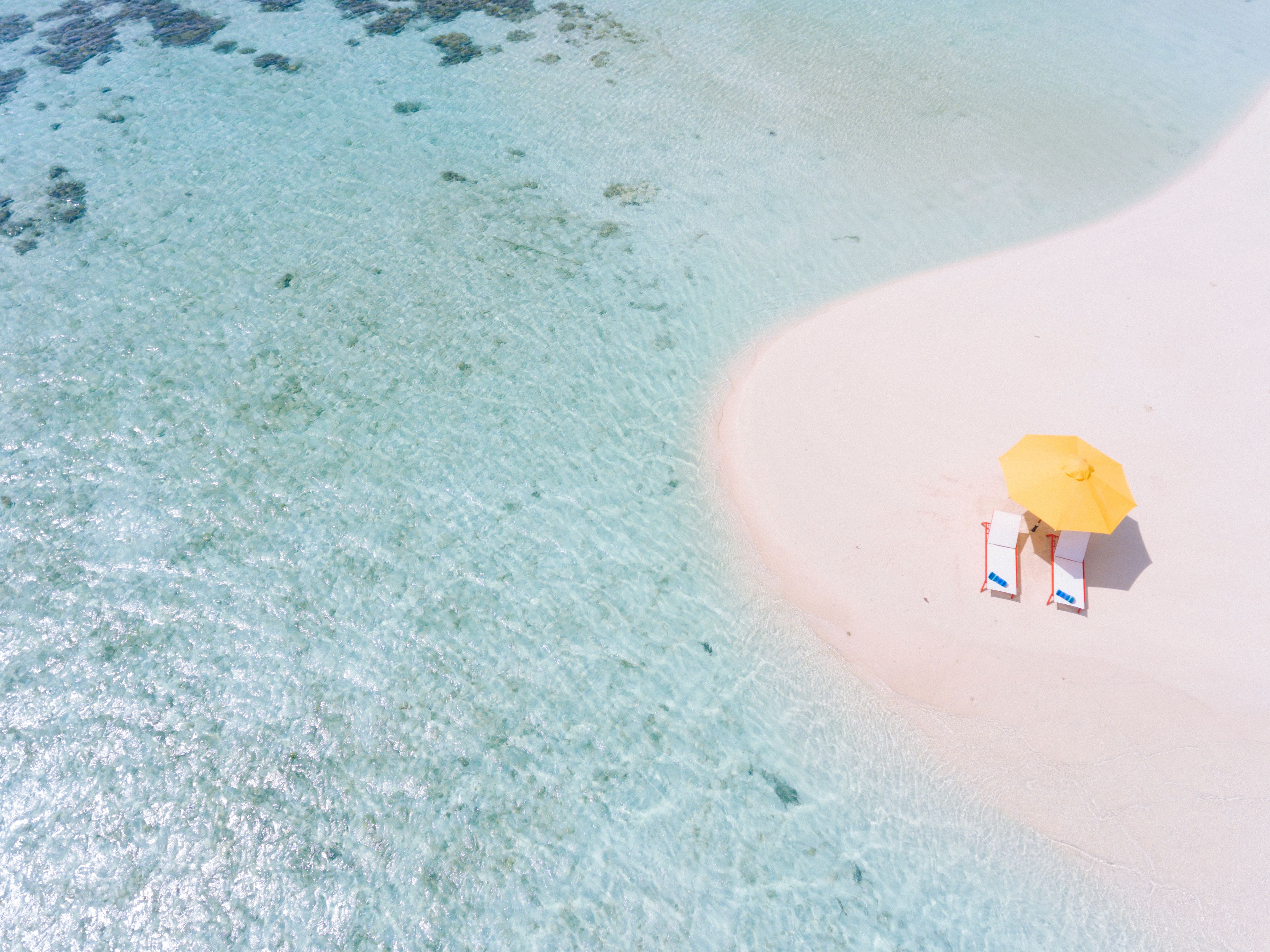 Une plage avec une eau claire et une personne se trouvant sous un parasol jaune.