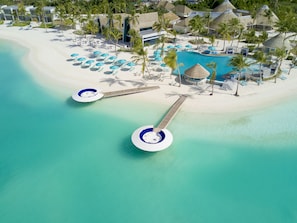 An aerial view of a resort with a large pool, multiple beachside umbrellas, and palm trees. - Kandima Maldives (Kandima Island)