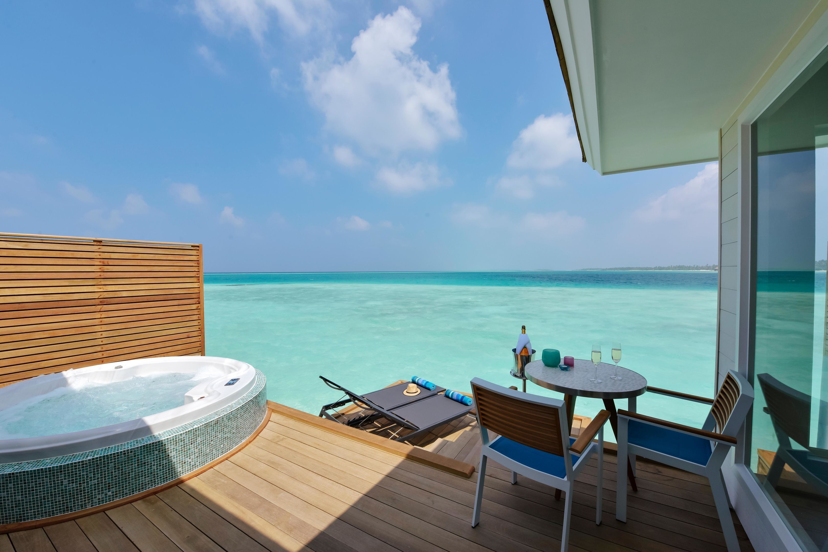 A wooden deck with a hot tub, a table with chairs, and a view of the turquoise sea.
