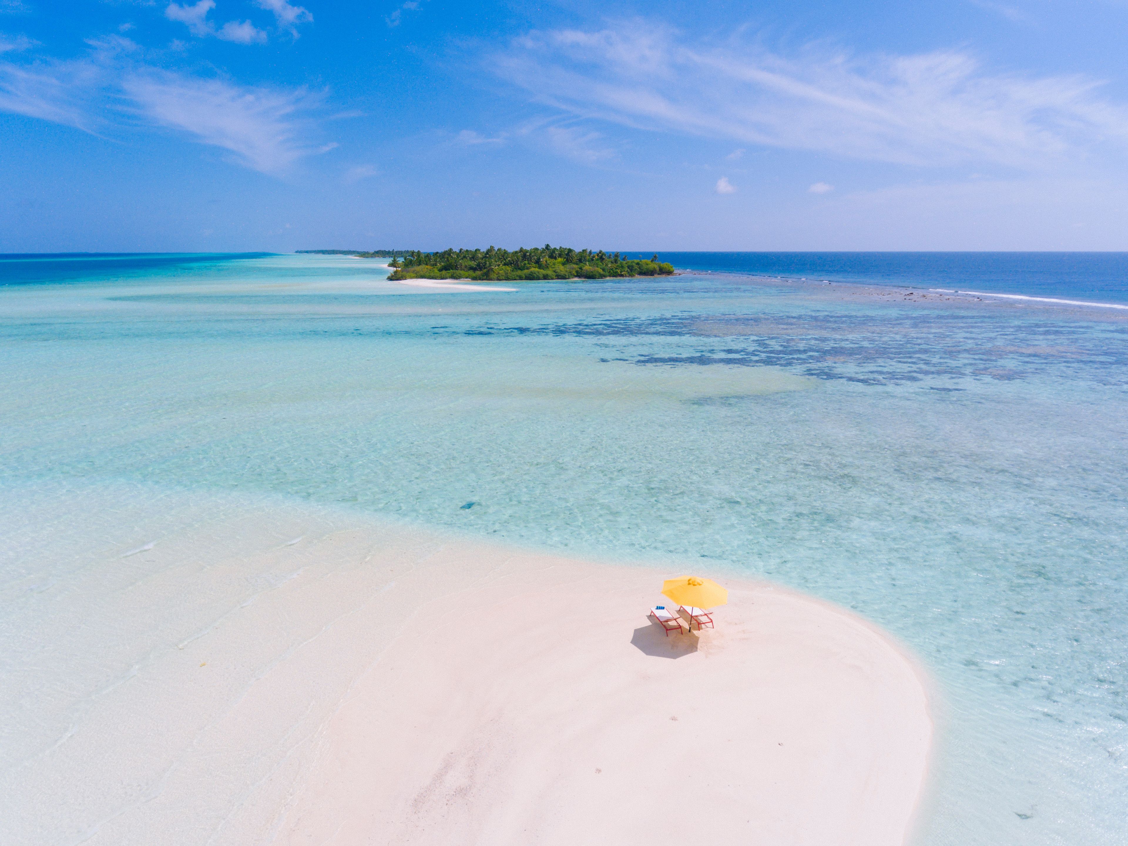 Una playa con agua turquesa cristalina, una orilla arenosa y una pequeña isla con vegetación en la distancia.