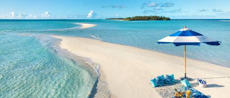 A beach with clear turquoise water, a sandy shore, and a blue and white umbrella.