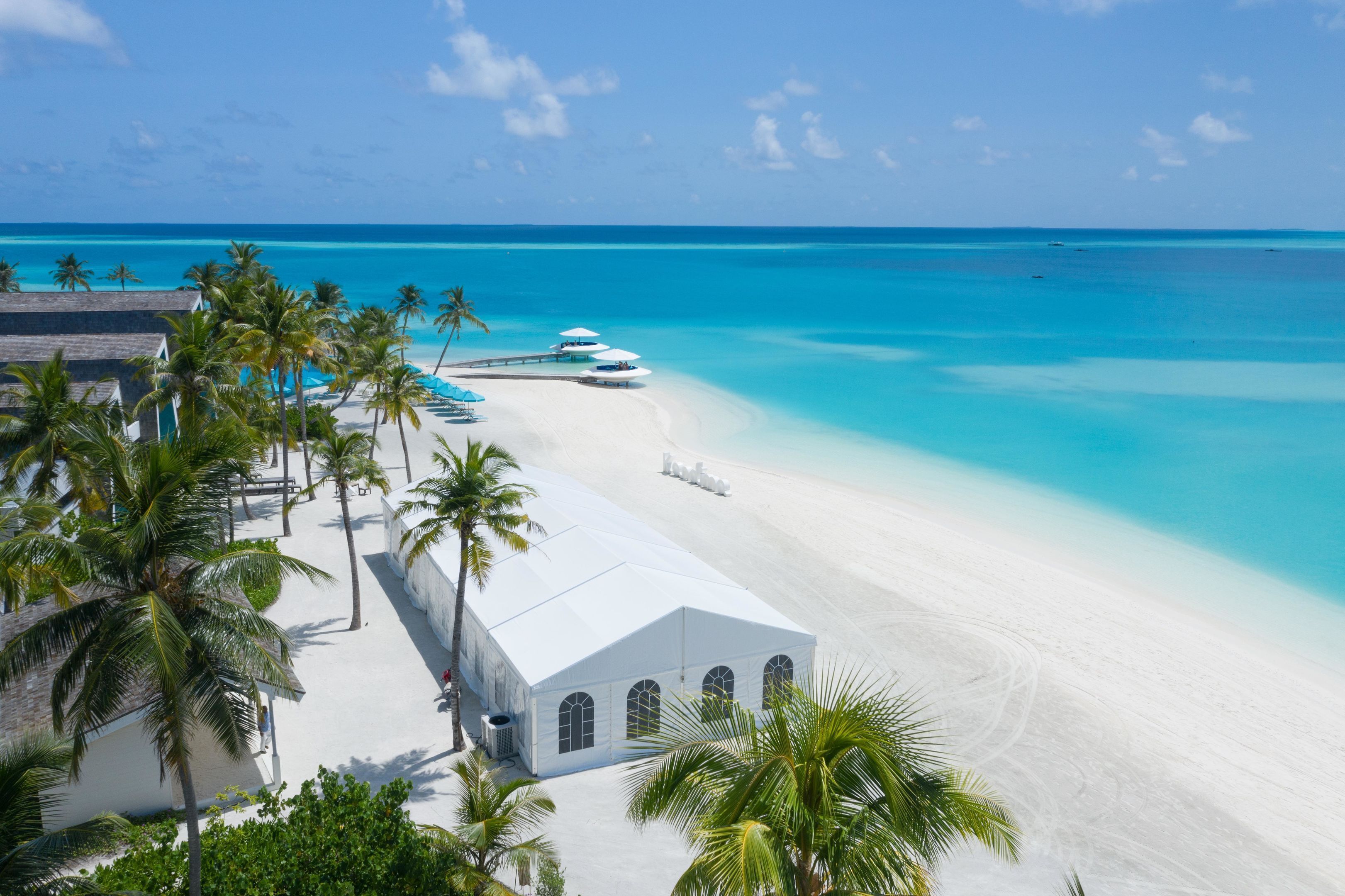 A beach resort with a white building, palm trees, and a pier extending into the turquoise sea.