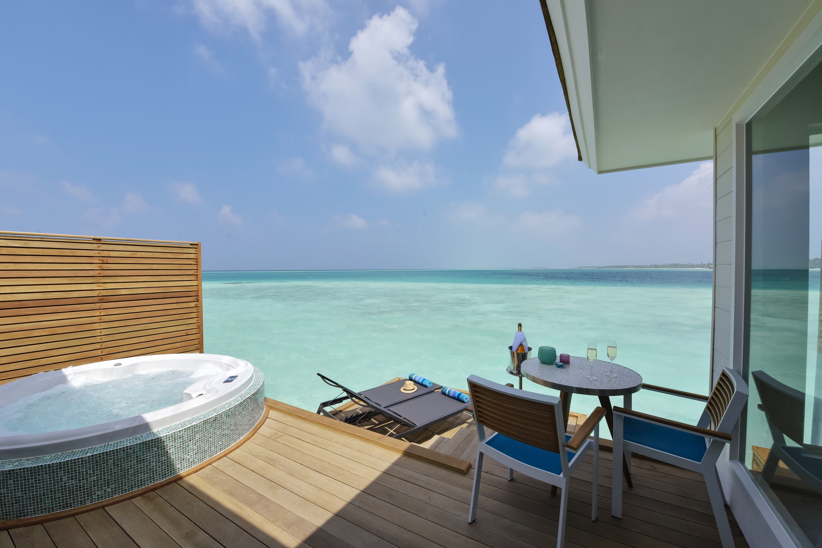 A deck with a hot tub, a table with chairs, and a view of the ocean.