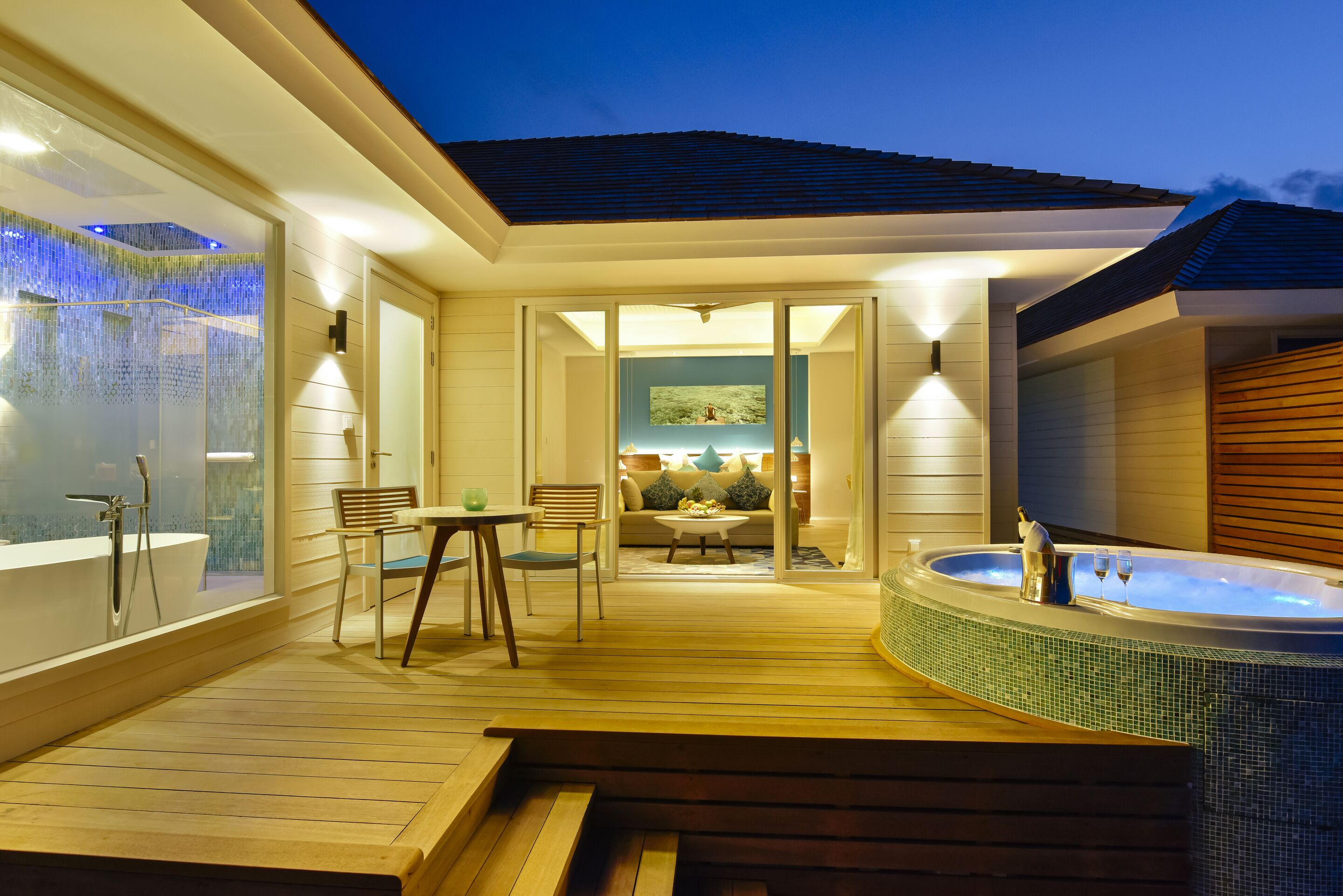 Una terraza moderna al aire libre con un jacuzzi, muebles de madera y una zona cerrada con paredes de vidrio que incluye una cascada.