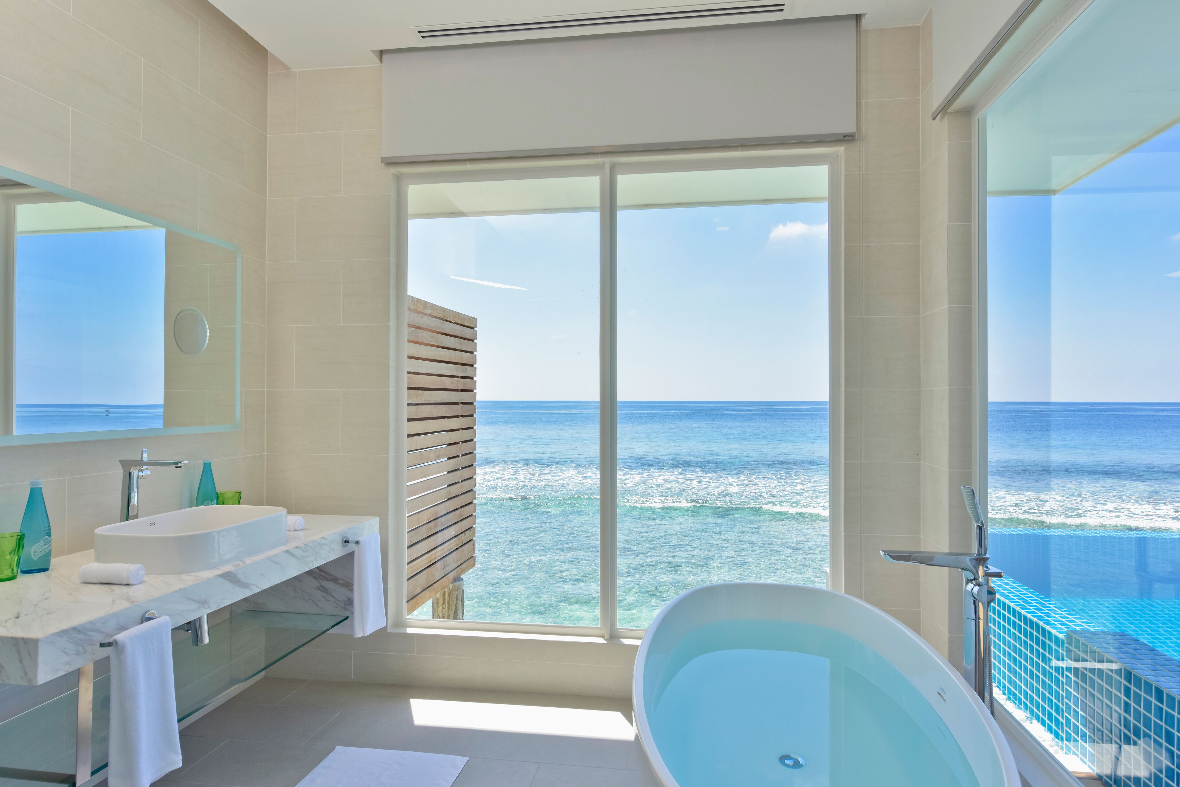 A modern bathroom with a large bathtub, a glass-enclosed shower, and a view of the ocean.