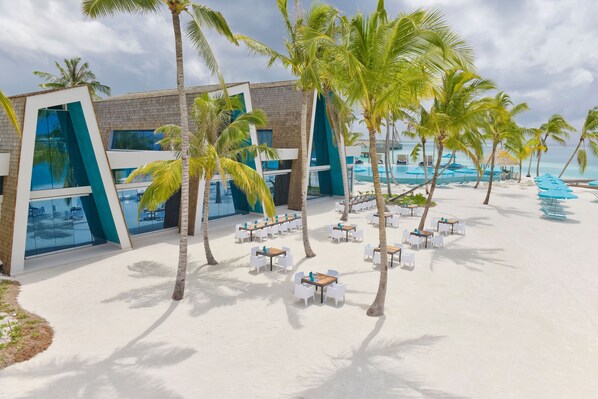 A beachside hotel with outdoor seating, palm trees, and a pool area. - Kandima Maldives (Kandima Island)