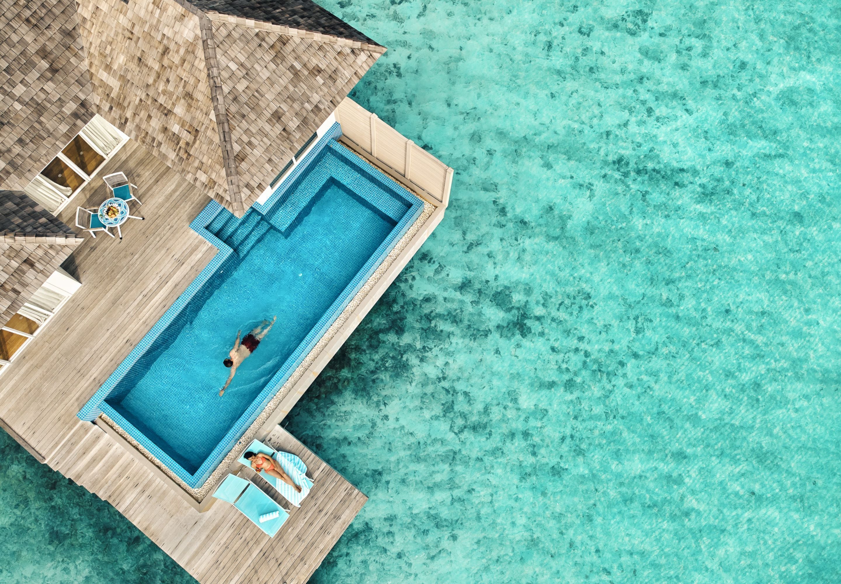 Vista aerea di un resort con piscina, terrazza in legno e poltrona relax.
