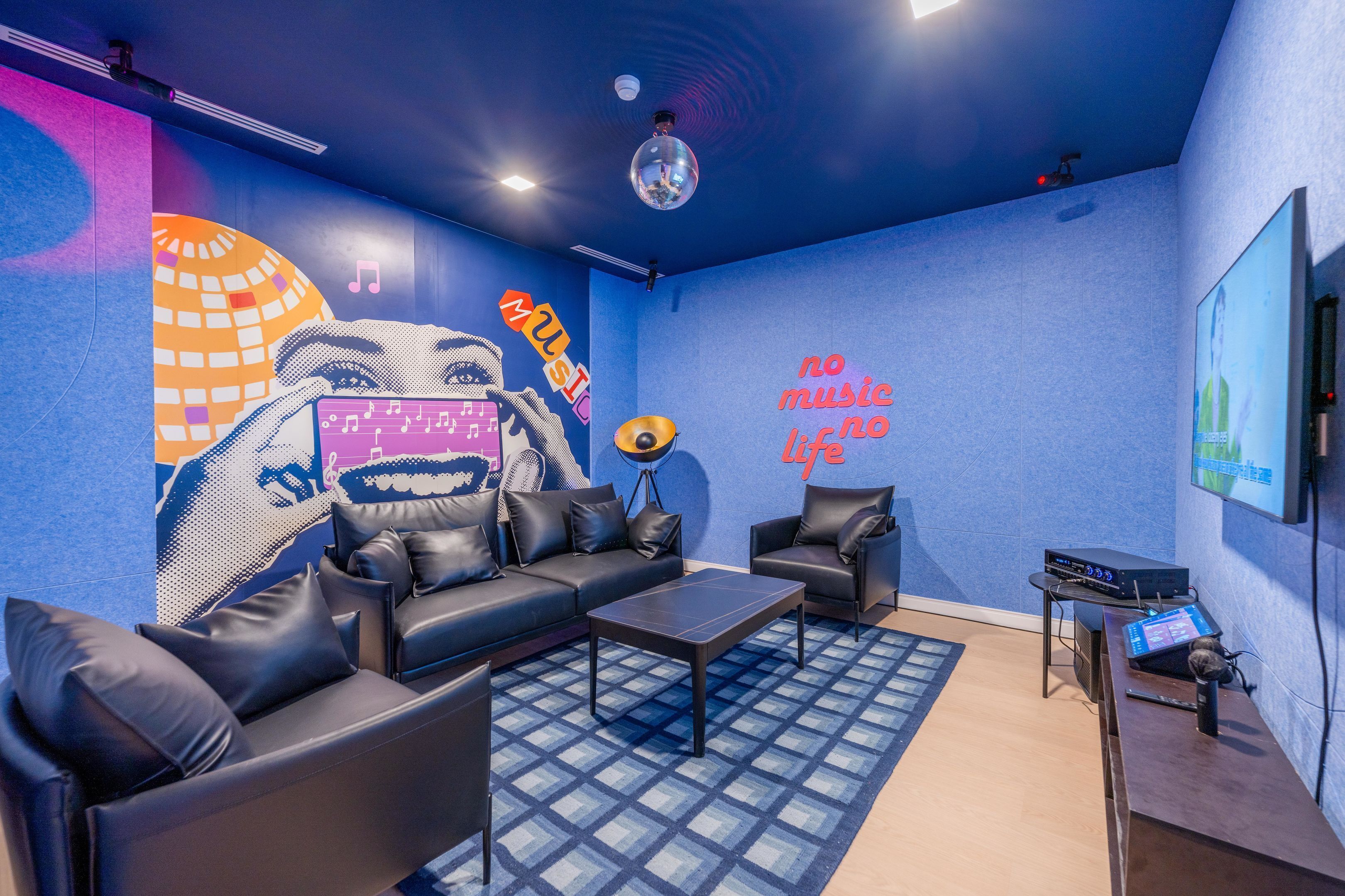 Una habitación moderna con pared azul, un mural grande, un sofá, una mesa de centro y equipo de DJ.