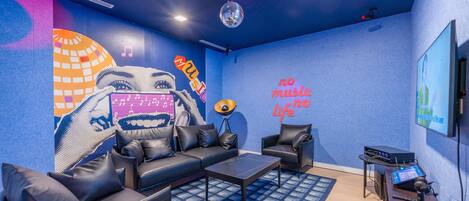 Una habitación moderna con pared azul, un mural grande, un sofá, una mesa de centro y equipo de DJ.