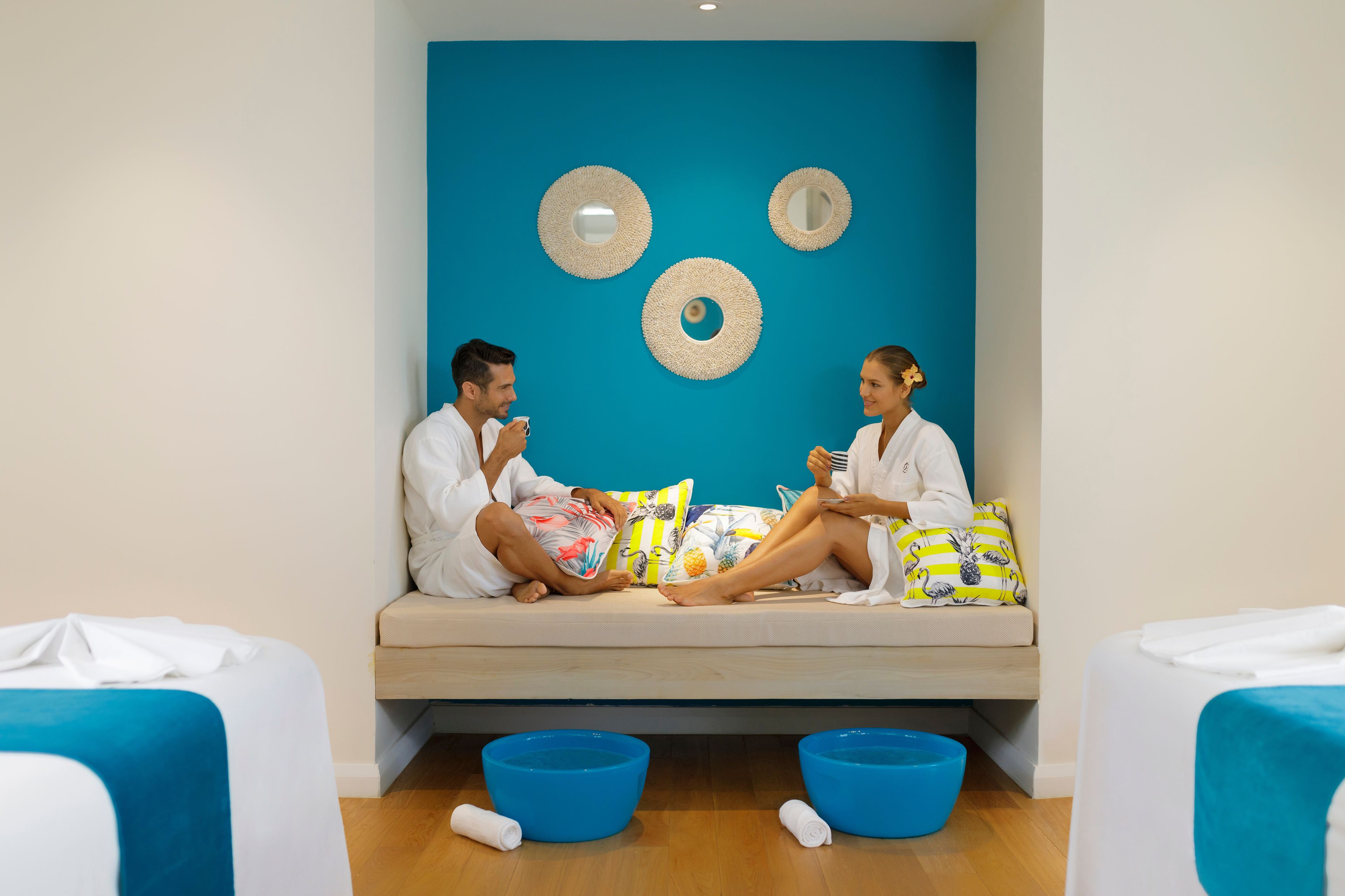 A room with a blue wall, two circular mirrors, and a sofa with colorful pillows.