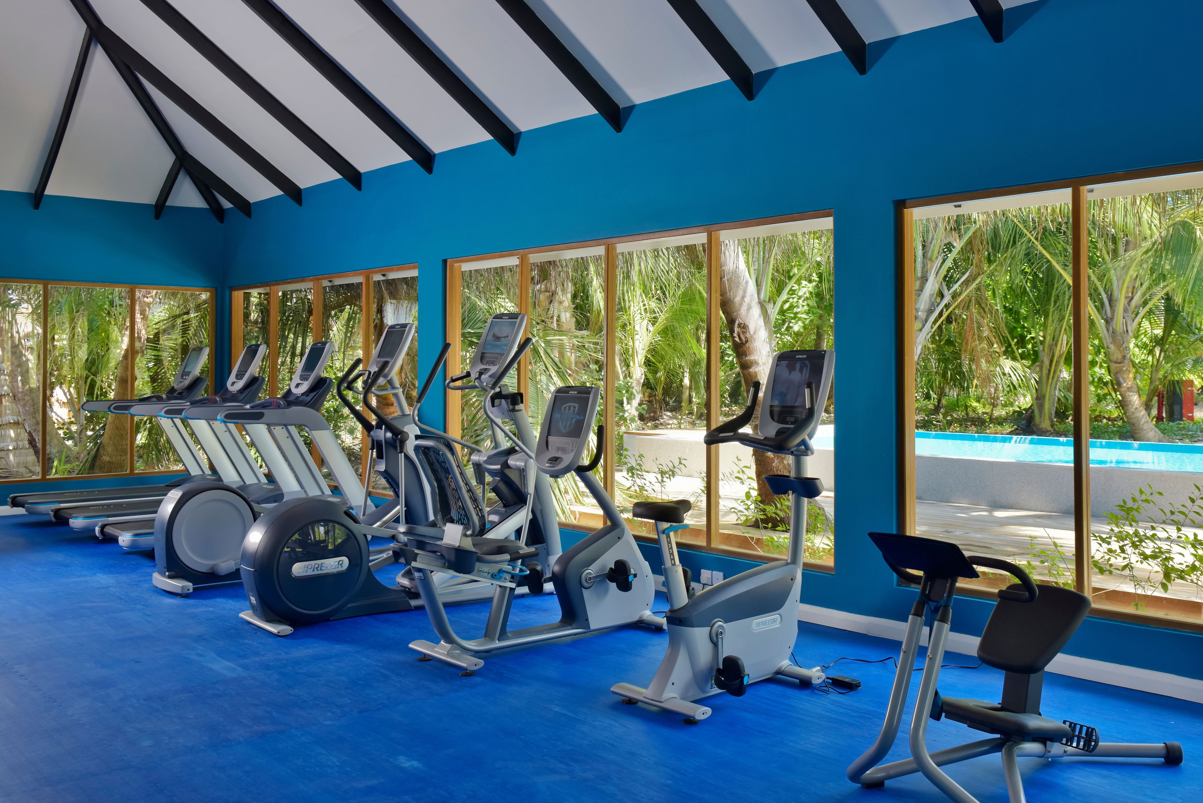 Un gimnasio con equipo de ejercicio, ventanas amplias y suelo azul.