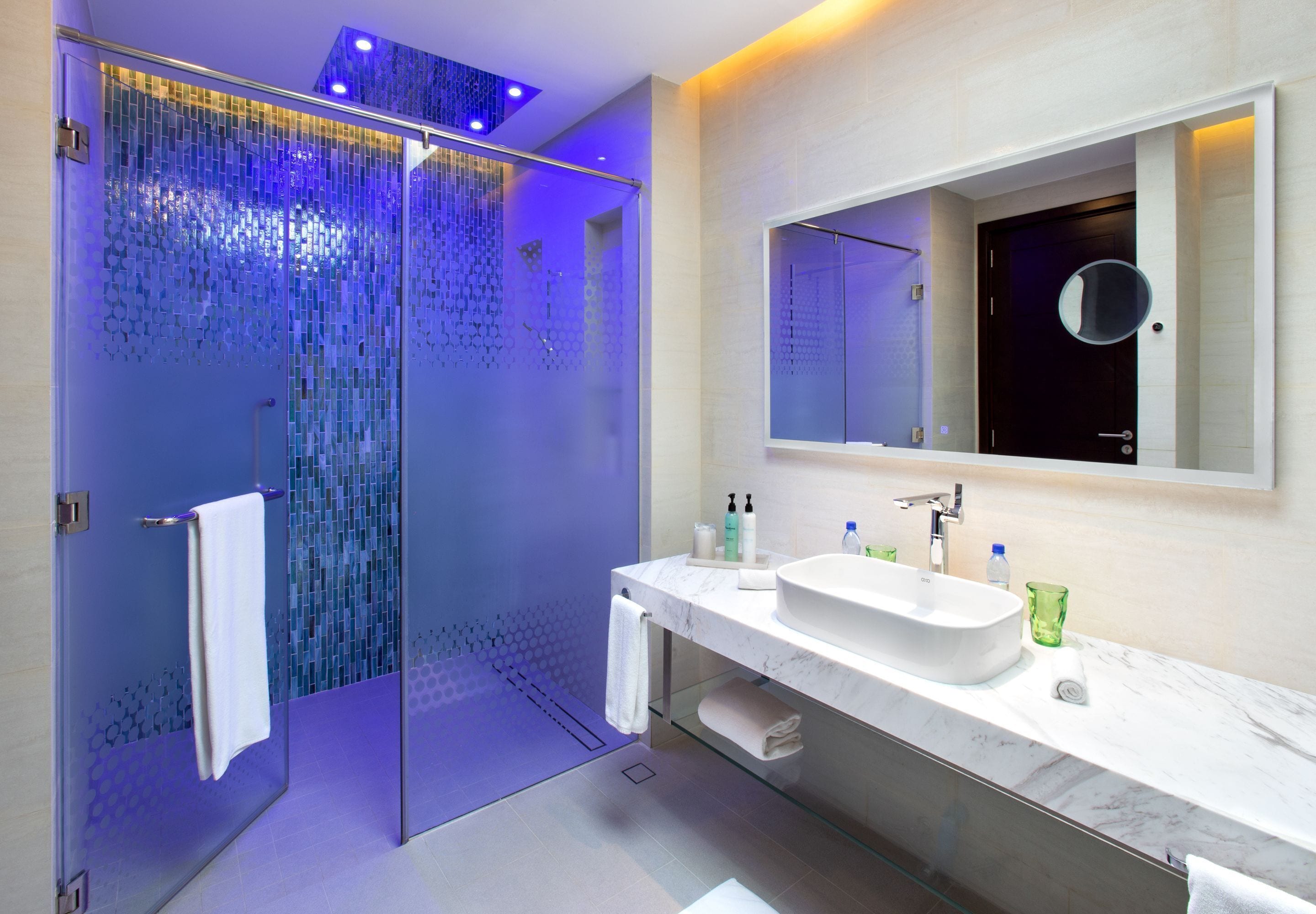 A modern bathroom with a glass-enclosed shower, a large mirror, and a marble vanity.