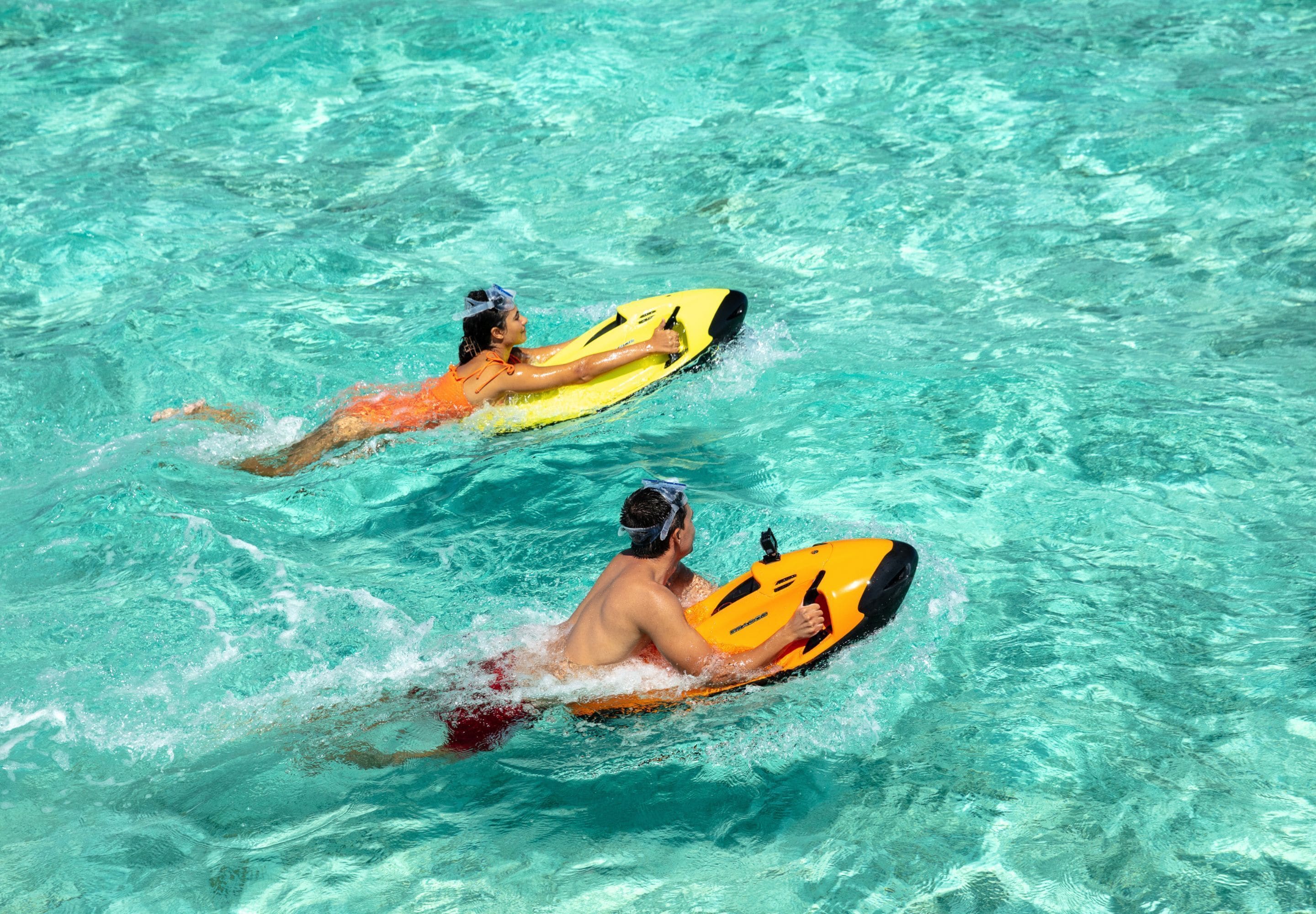 Zwei Personen auf einem gelben Wasserfahrzeug in klarem Wasser.