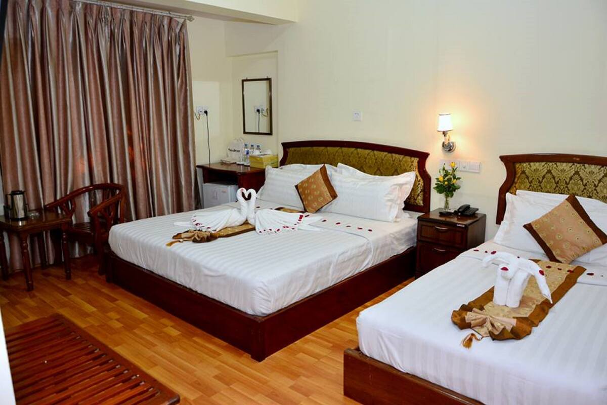 A hotel room with two beds, wooden headboards, a desk, and a chair.