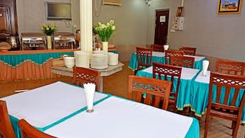 A dining area with tables set for guests, a buffet station with stacked plates, and a decorative vase with flowers.