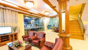 A spacious living room with leather sofas, a glass coffee table, and a television. A wooden column and staircase are visible in the background. - Hotel Wonderland (Mandalay)