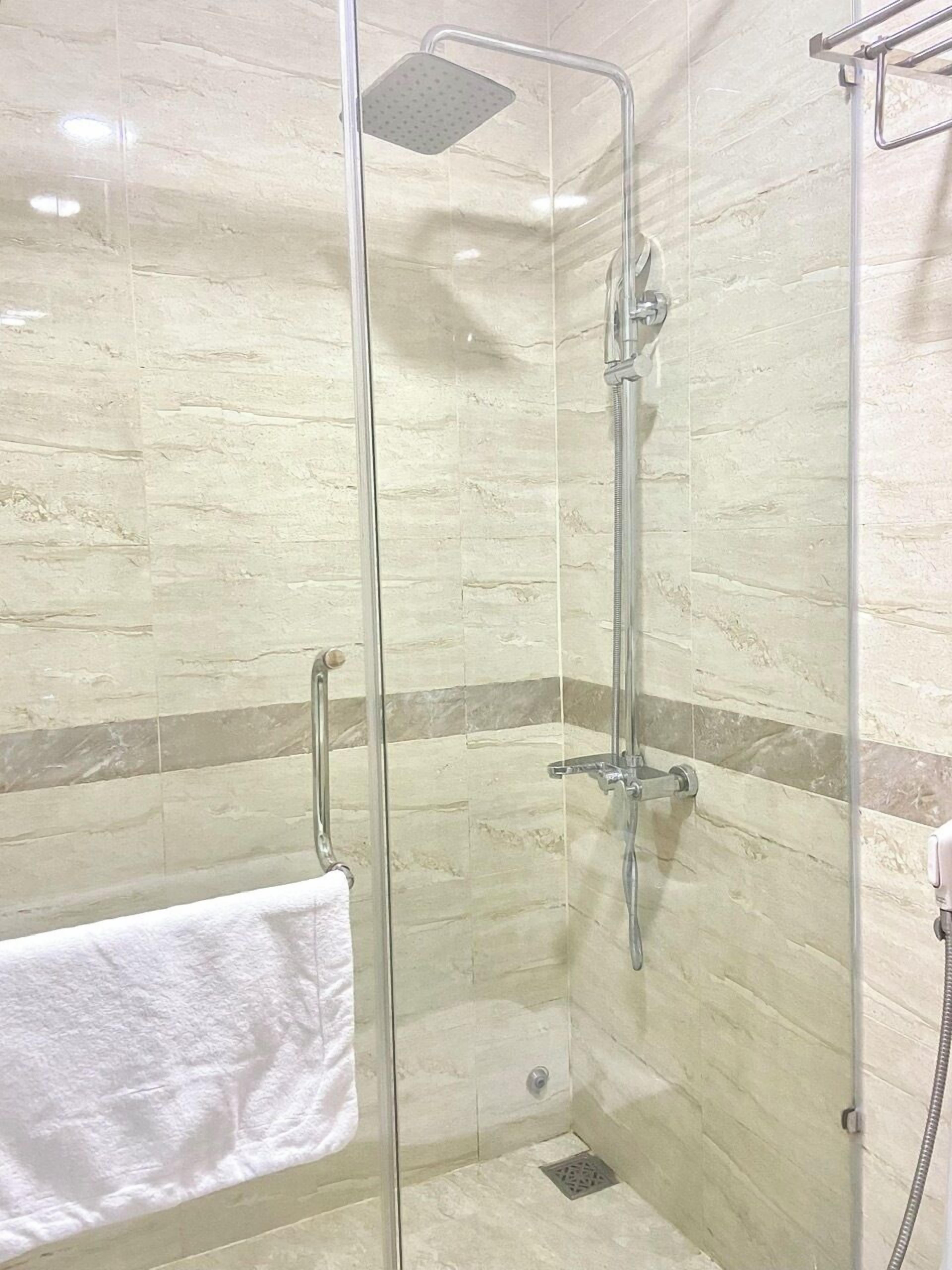 A glass-enclosed shower with a handheld showerhead and a wall-mounted faucet.