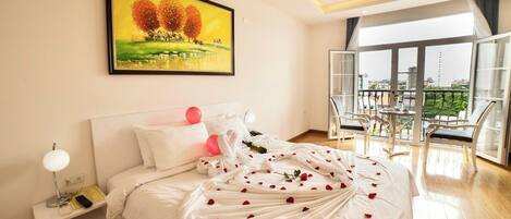 A hotel room with a bed, a nightstand, a painting, and a balcony with chairs.