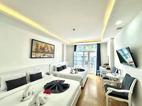 A hotel room with two beds, a TV, a small table, and a balcony with a view.