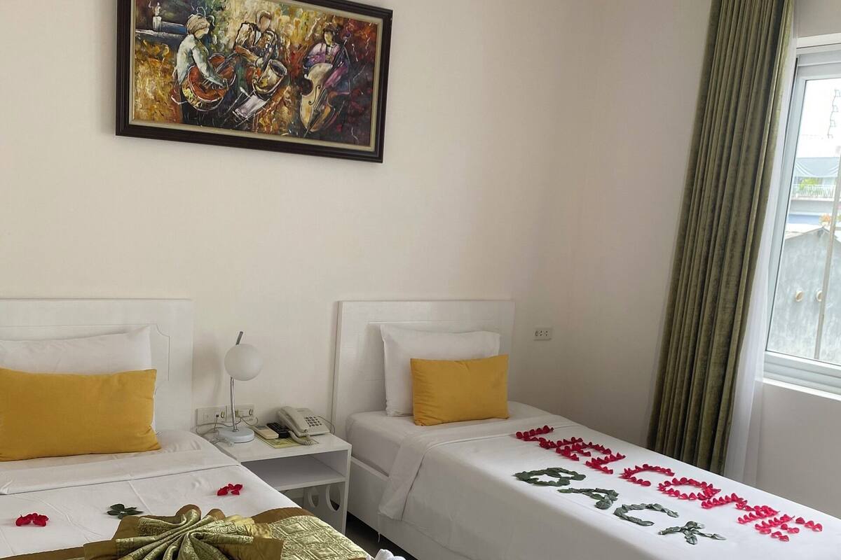 A hotel room with two beds, a painting on the wall, and a window with curtains.