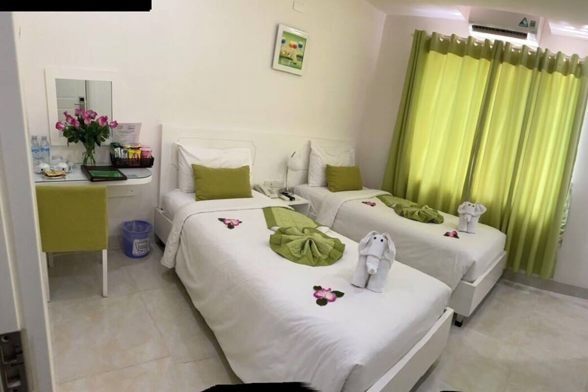 A hotel room with two beds, a desk, a mirror, a TV, and a green curtain.