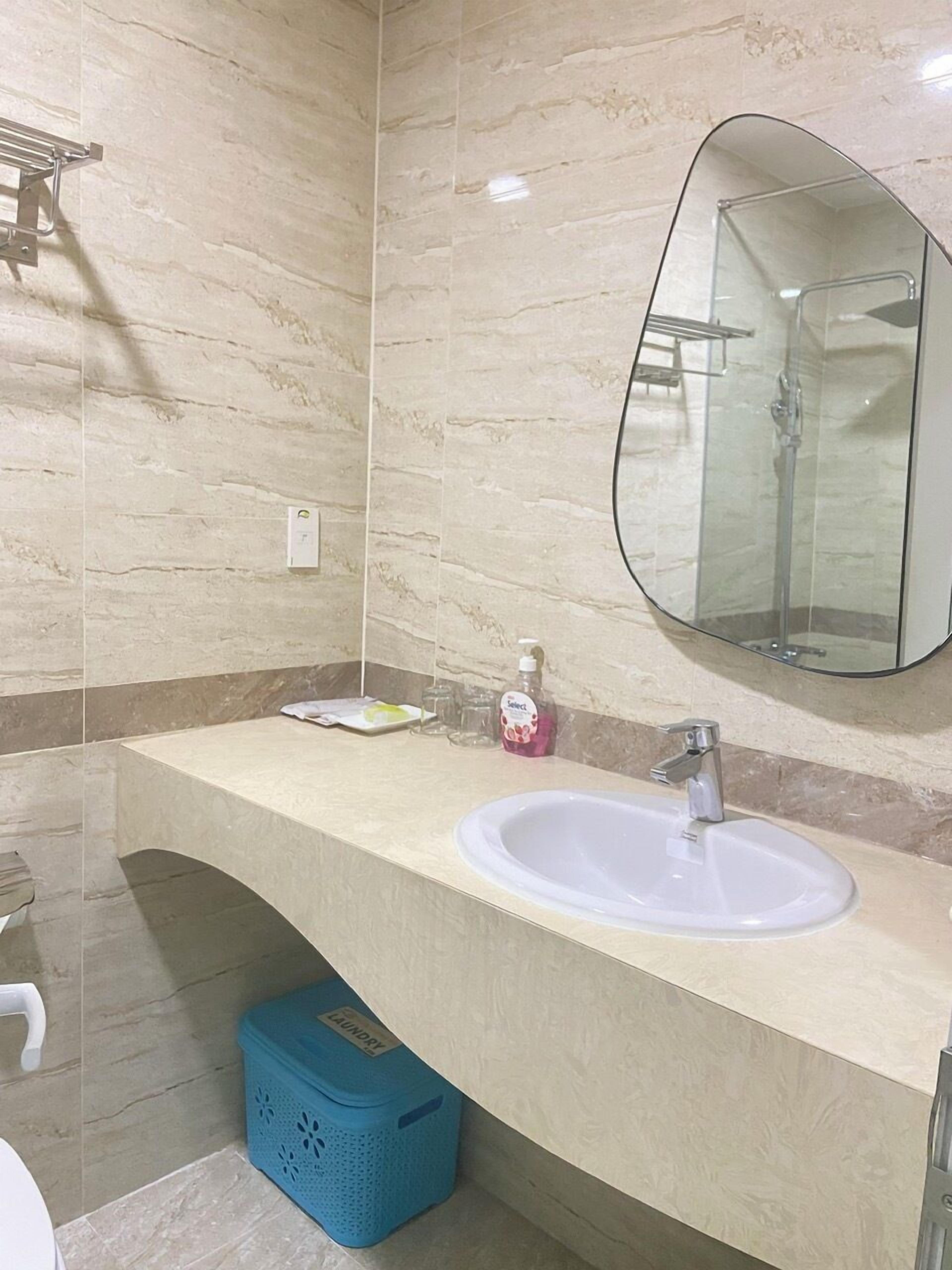 A bathroom with a marble wall, a white sink, a mirror, and a shower enclosure.