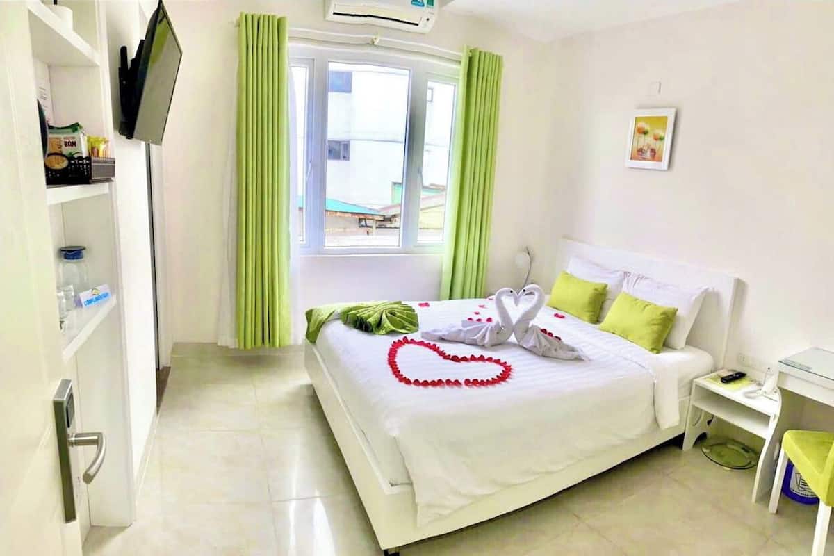 A hotel room with a bed, a desk, a chair, a TV, and a window with curtains.