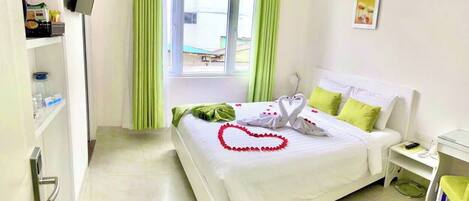 Habitación de hotel con cama, escritorio, silla, televisor y ventana con cortinas.