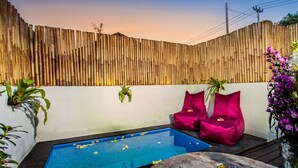 A pool area with a bamboo wall, two red cushioned chairs, and a small table with a glass bowl. - Svaha Private Villas Ceningan (Ceningan Island)