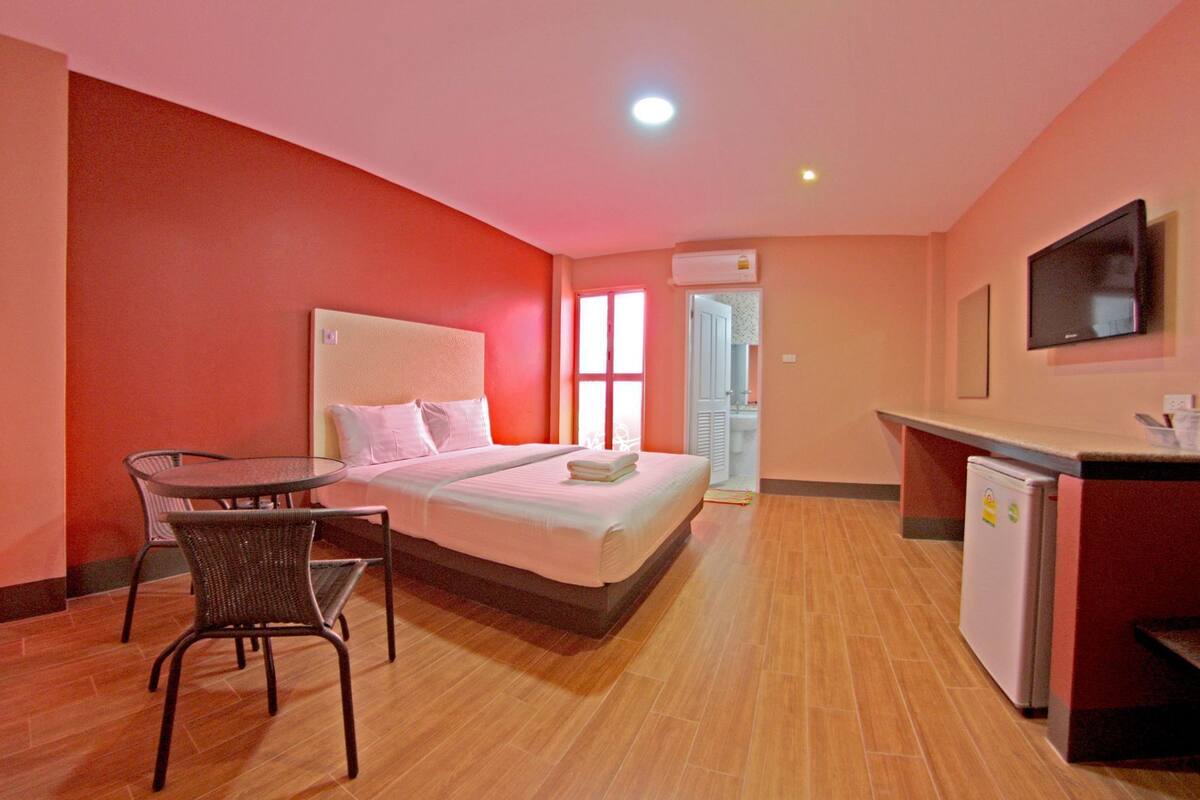 A hotel room with a bed, a small table with chairs, a refrigerator, and a TV mounted on the wall.